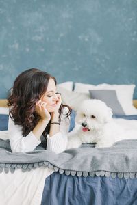 Young woman looking at poodle puppy while lying on bed at home
