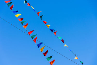 Low angle view of colorful buntings hanging against clear blue sky