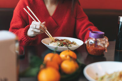 Young asian woman in red clothes eating asian food with bamboo chopsticks in chinese restaurant