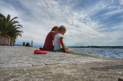 Girl sitting with sister by sea