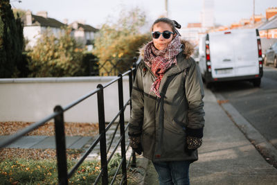 Portrait of young woman standing by railing on sidewalk