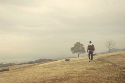 Rear view of man walking on field against sky