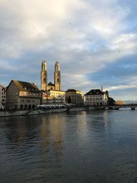 View of buildings by river against cloudy sky