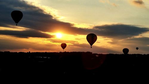 Silhouette hot air balloons flying against sky during sunset