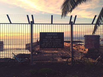 Warning sign on railing against sky during sunset