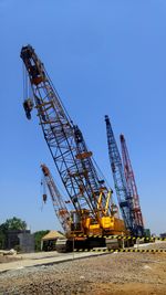 Low angle view of cranes at construction site against sky