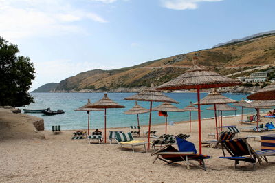 Sunshades and lounge chairs on beach against sky