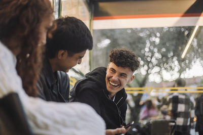 Happy boy laughing with friends while sitting at bus stop
