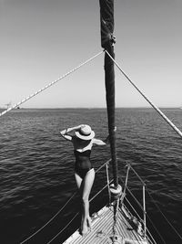 Woman wearing bodysuit standing on boat in sea against sky