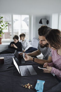Mother and father shopping online with sons in living room at home