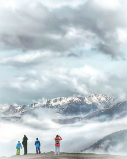 Rear view of people standing on snowcapped mountain against sky