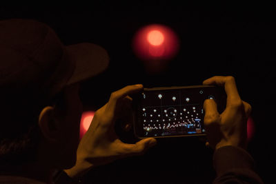 Man photographing illuminated lights through mobile phone at night