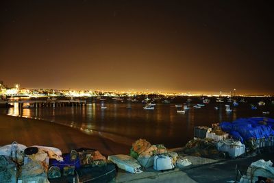 Illuminated city by river against sky at night