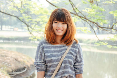 Portrait of smiling young woman against trees