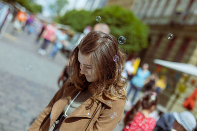 Young woman wearing overcoat while standing with bubbles on street