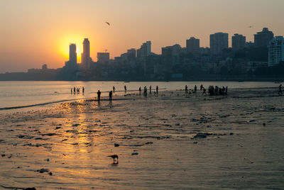 Group of people on beach in city at sunset
