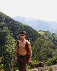 Shirtless muscular young man standing against mountains