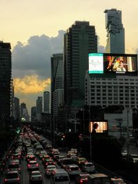 Traffic on road amidst buildings in city during sunset