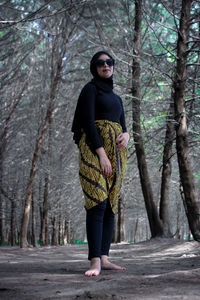 Portrait of woman standing by tree trunk in forest
