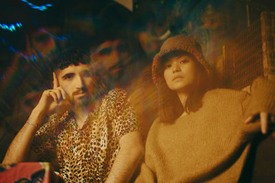 Multiple exposure of young male and female friends sitting together at illuminated restaurant