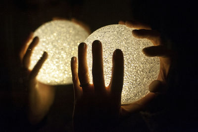 Close-up of human hands holding illuminated balls in darkroom