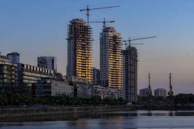 Modern buildings by river against sky in city