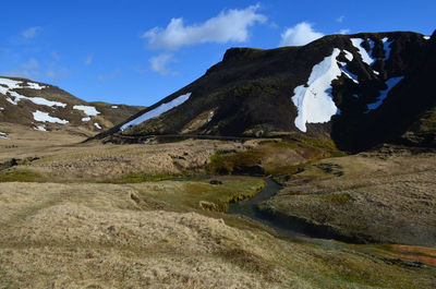 Landscape with a hot spring river and snow on surrounding mountain sides.