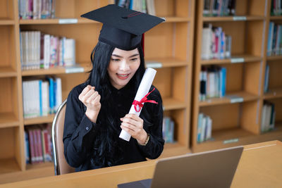 Young woman holding diploma at library