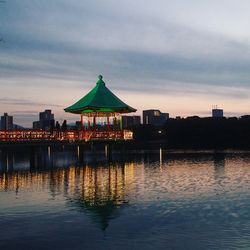 Illuminated building at waterfront during sunset