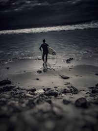 Rear view of man with surfboard walking at beach