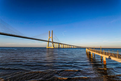 Bridge over calm sea against clear blue sky