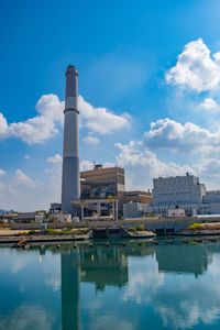 Factory by river against sky in city