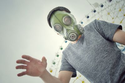 Low angle portrait of man wearing gas mask against ferris wheel