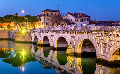 Arch bridge over river by buildings against sky in city