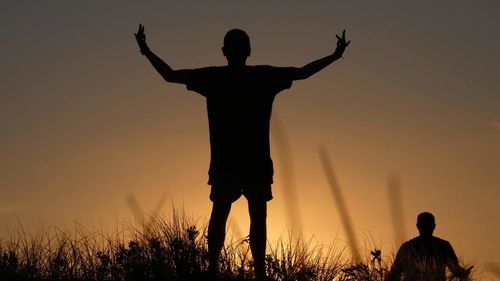 Silhouette men standing on field against sky during sunset