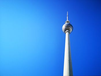 Low angle view of communications tower in city against clear blue sky