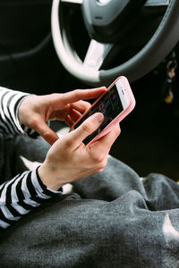 Portrait of a young brunette woman driving in a car using a smartphone