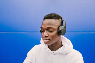 Portrait of young man wearing headphones against blue wall
