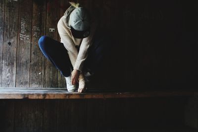 Full length of woman sitting on wood against wall