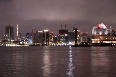 Illuminated buildings by sea against sky at night