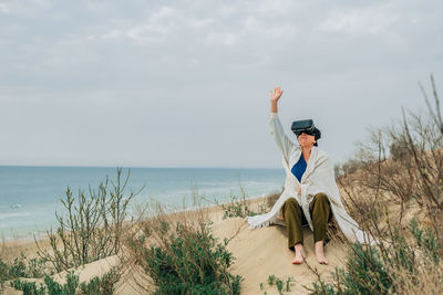 An adult woman on a sandy beach in spring wearing vr virtual reality glasses in front of her eyes