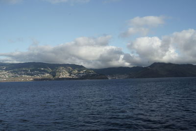 Scenic view of sea by mountain against sky