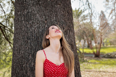 Smiling woman standing against tree trunk on land 