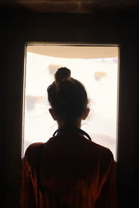 Rear view of woman looking through window at home