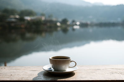 A cup of coffee on a rustic wooden table with village blurred background.