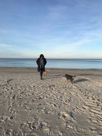 Full length of woman with dogs at beach against sky