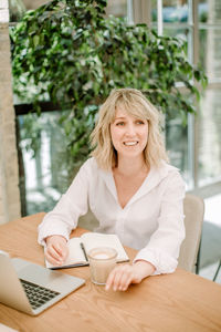 Smiling young woman using phone while sitting on table