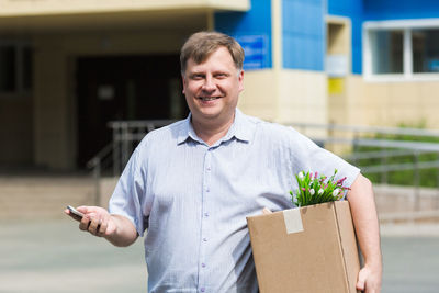 An adult man with a box of personal belongings calls on phone about getting a new job.