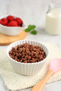 Bowl with chocolate rice crispy cereal for breakfast. served with milk and raspberry