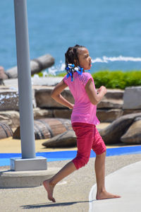 Side view of wet girl running on walkway during sunny day